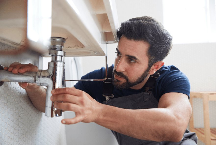 male plumber working to fix leaking sink in home bathroom