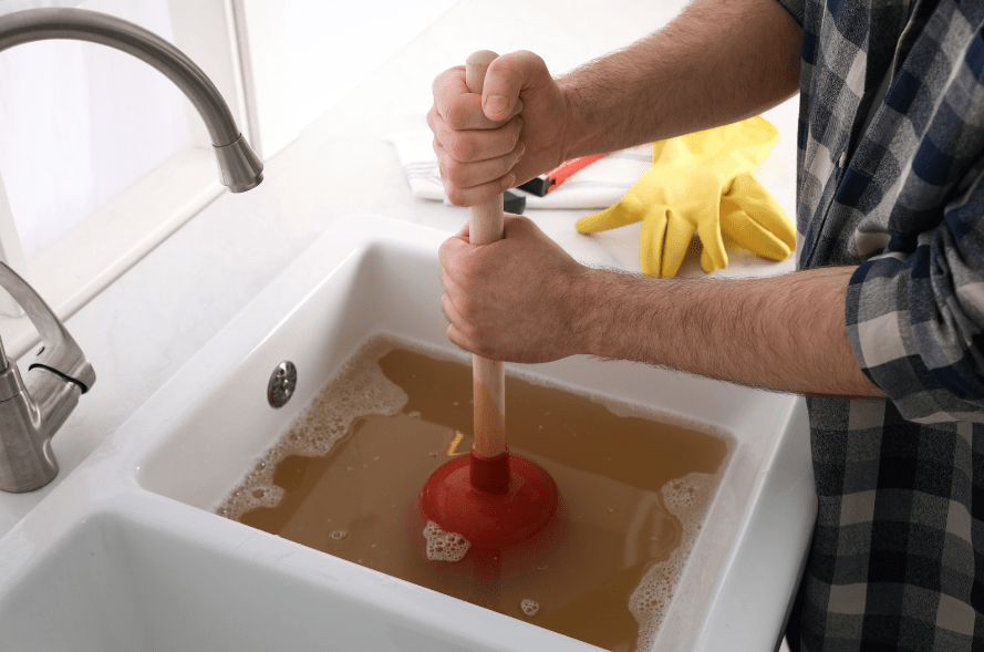 man using plunger to unclog sink drain in kitchen